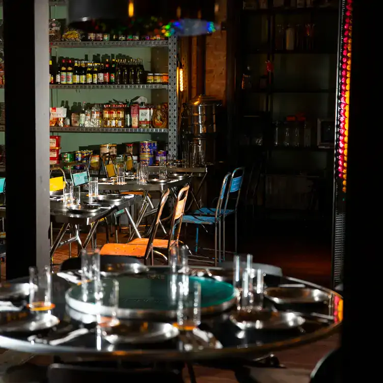 The interior dining space of Double Rainbow Bar & Eating House with metal chairs and tables and shelves stacked with different ingredients along one wall.