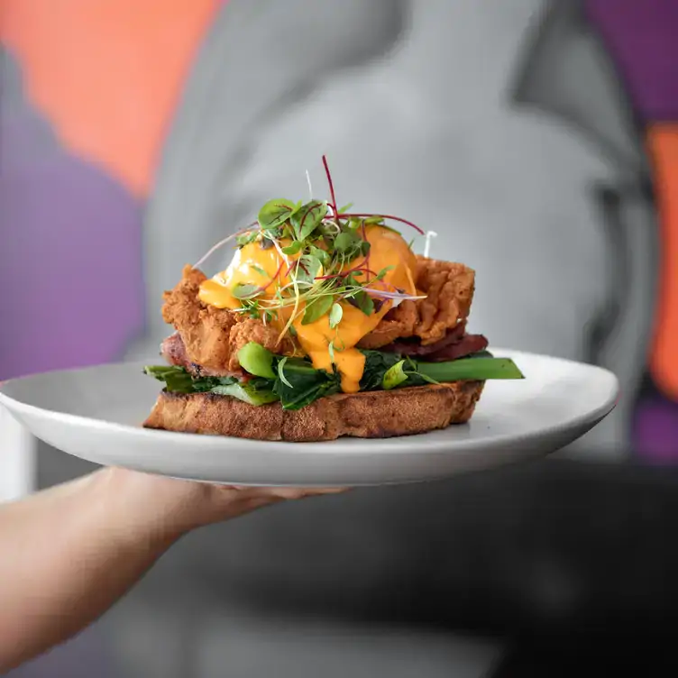 Someone carries a dish of eggs benedict on fried chicken and toast served at Todd and Pup, one of Brisbane’s best pubs.