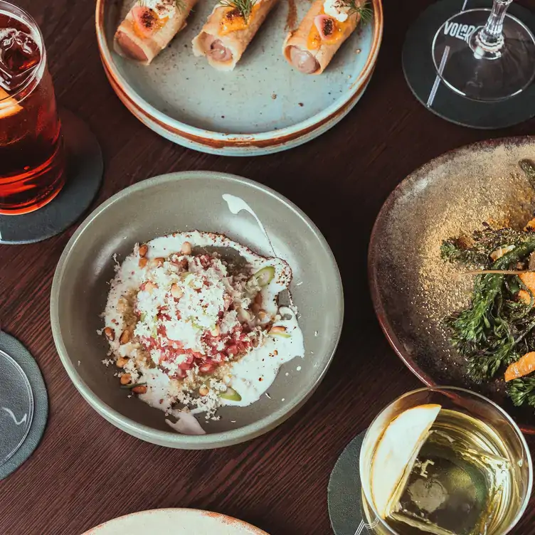 Several dishes including salads served alongside cocktails at Volare.