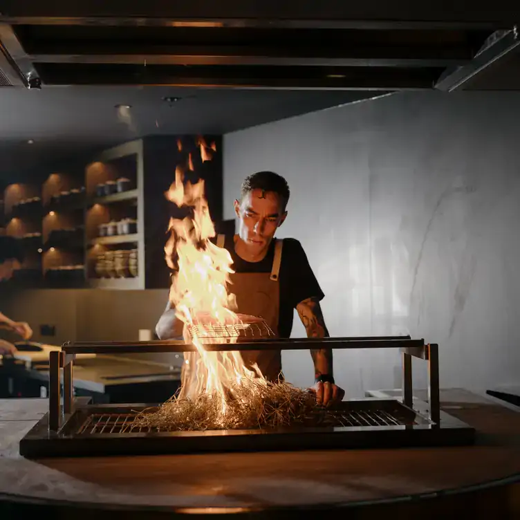 Someone cooks fish on a metal grill over large flames from dry grass that’s been set alight underneath it at Izakaya Público, one of the best pubs in Brisbane.