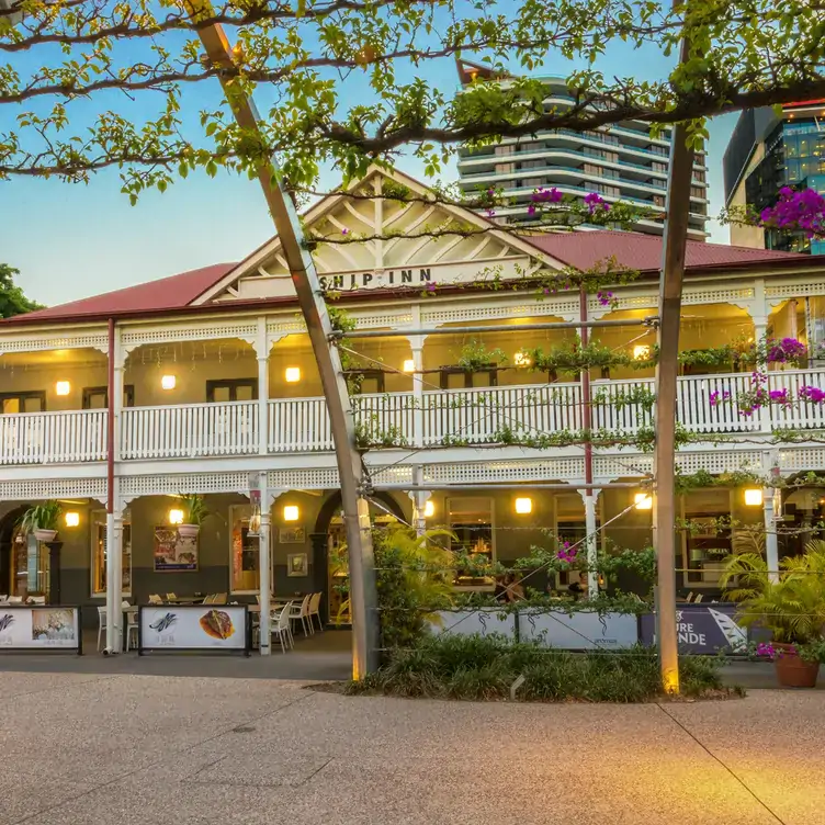 The exterior of The Ship Inn, showing the sheltered outdoor seating area, white fencing, red roof and surrounding greenery.