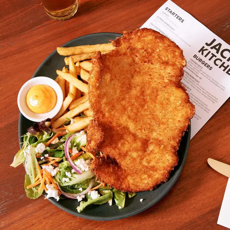 A plate of chicken schnitzel, chips and salad on top of a menu at Jack’s on Unley one of the best pubs in Adelaide.