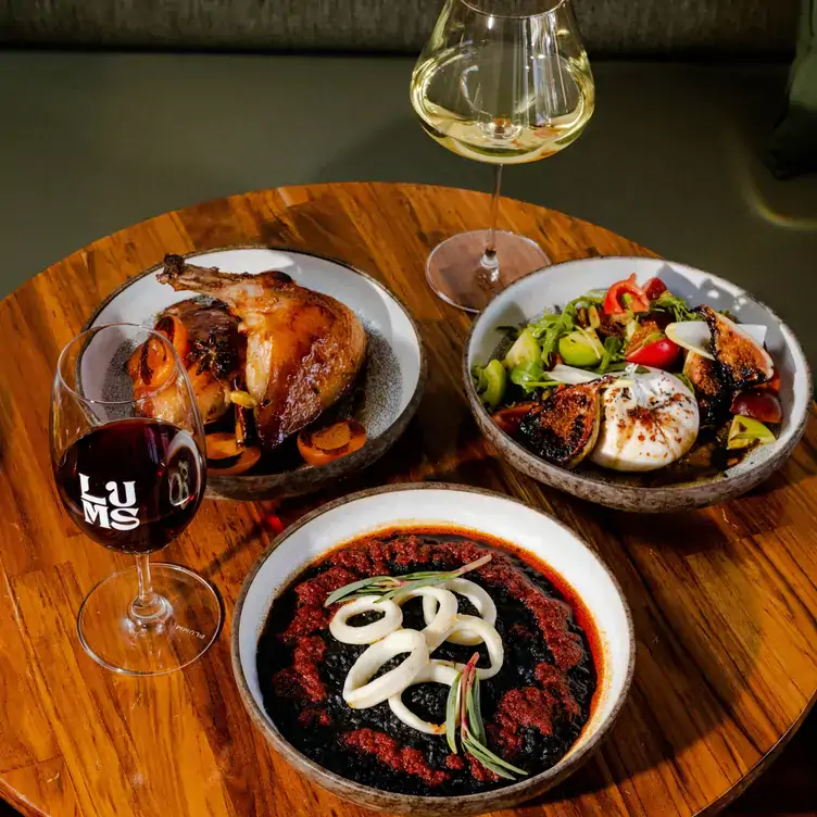 A table laid with multiple dishes including salad and a roast served alongside glasses of red and white wine at Lums Wine Bar.