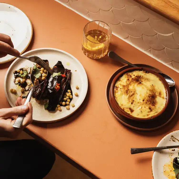 A diner picks a chickpea dish up with a spoon from a table with a cocktail and a pie at Olive, one of Adelaide’s best restaurants.