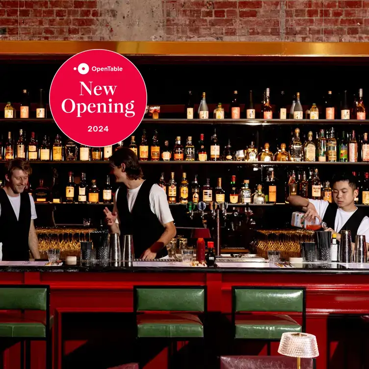 A team of bartenders at work behind a red bar featuring bottles lined up on shelves and exposed brick walls at Suzie Q in Melbourne.