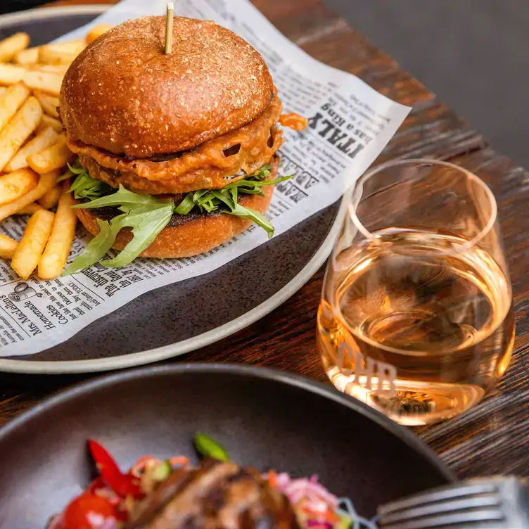 A burger and fries on newspaper with a drink, served at Customs House Bar, one of the best affordable restaurants in Sydney CBD.