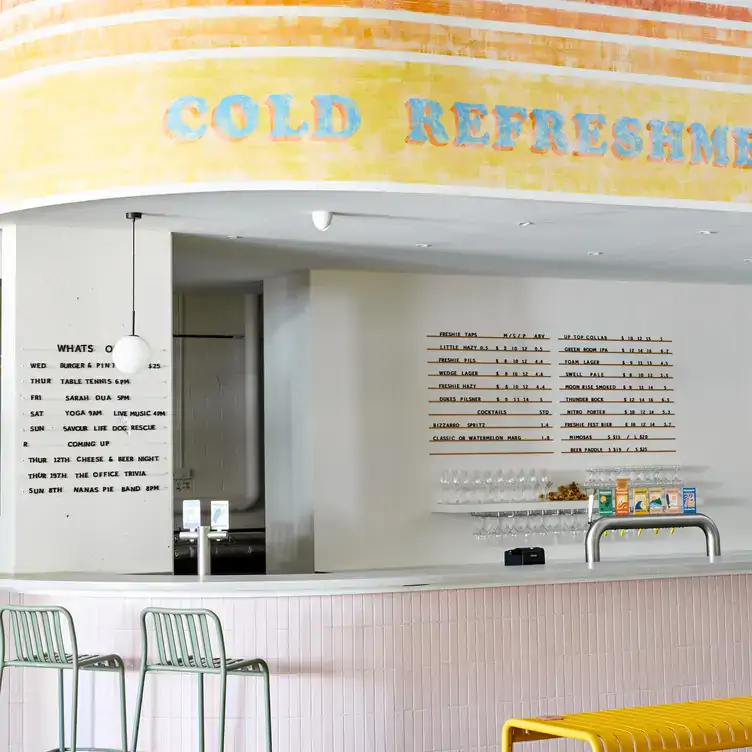 The bar at Freshwater Brewing Company, with pink tiles around the outside and yellow and blue on the wall above.