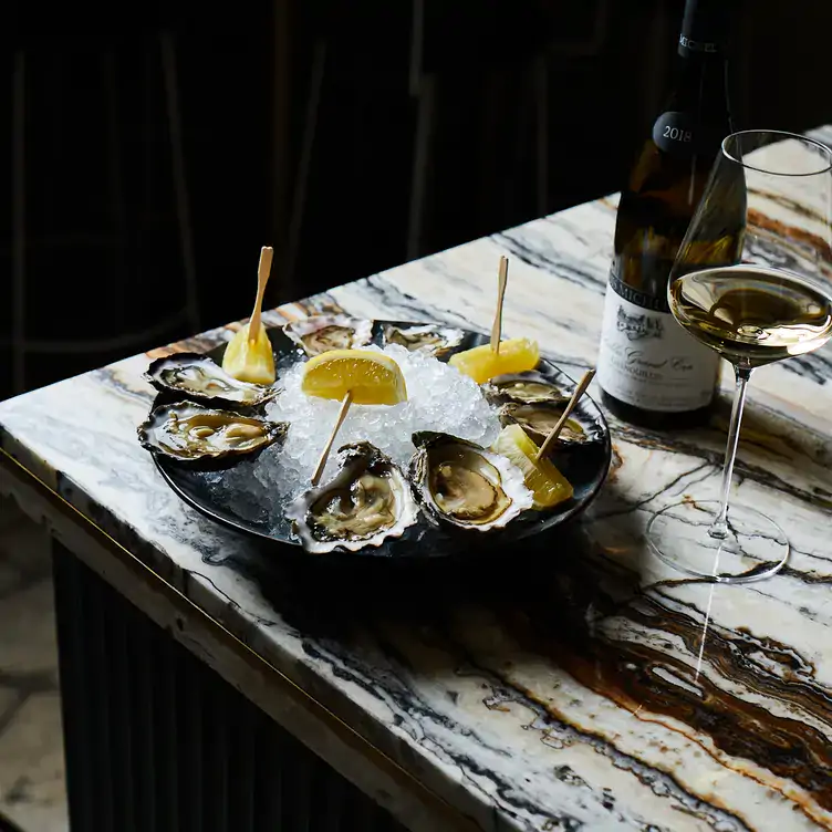 A plate of oysters and lemon on a bed of ice, served alongside white wine at Pearl Chablis and Oyster Bar, one of the best date night restaurants in Melbourne.