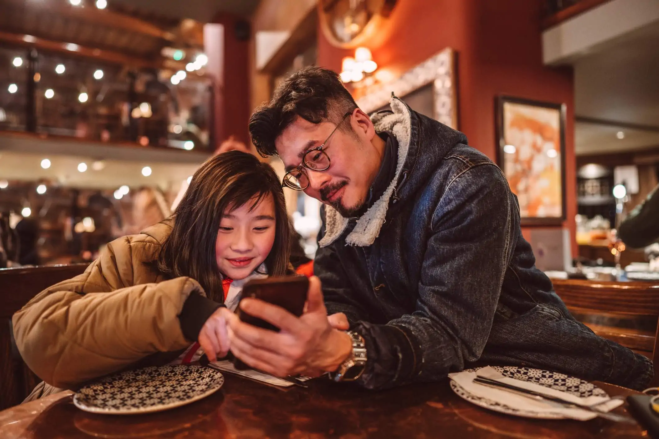 Two diners are looking at their mobile phone while seating in a restaurant