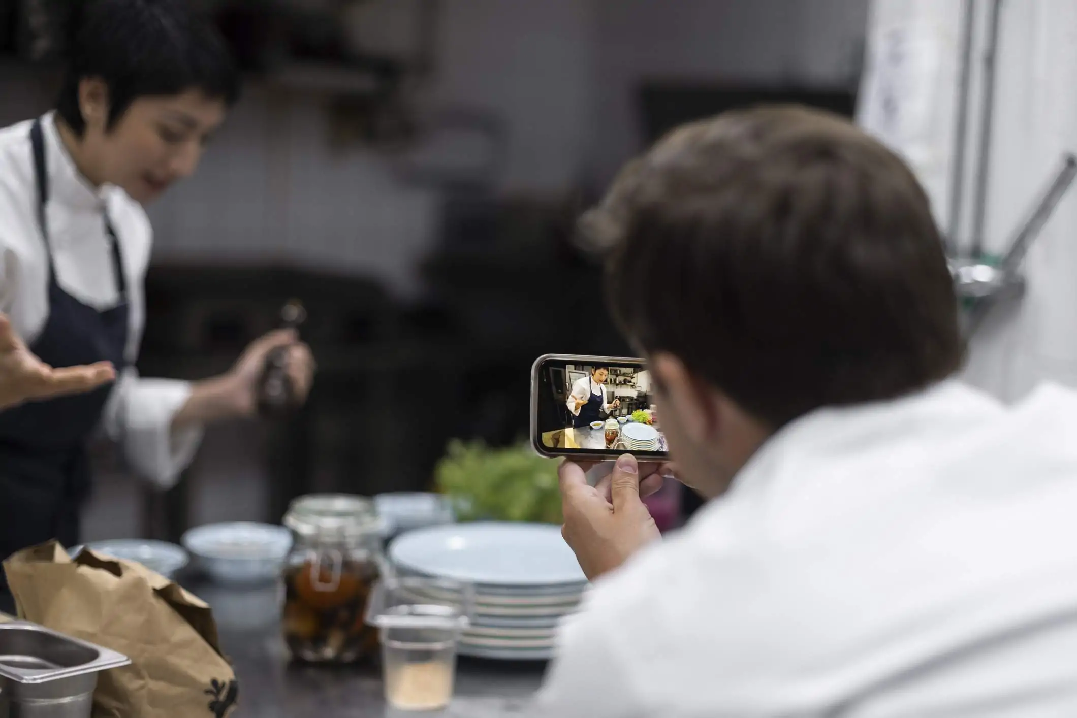 Image depicts a restaurant worker taking a video of another employee for social media.