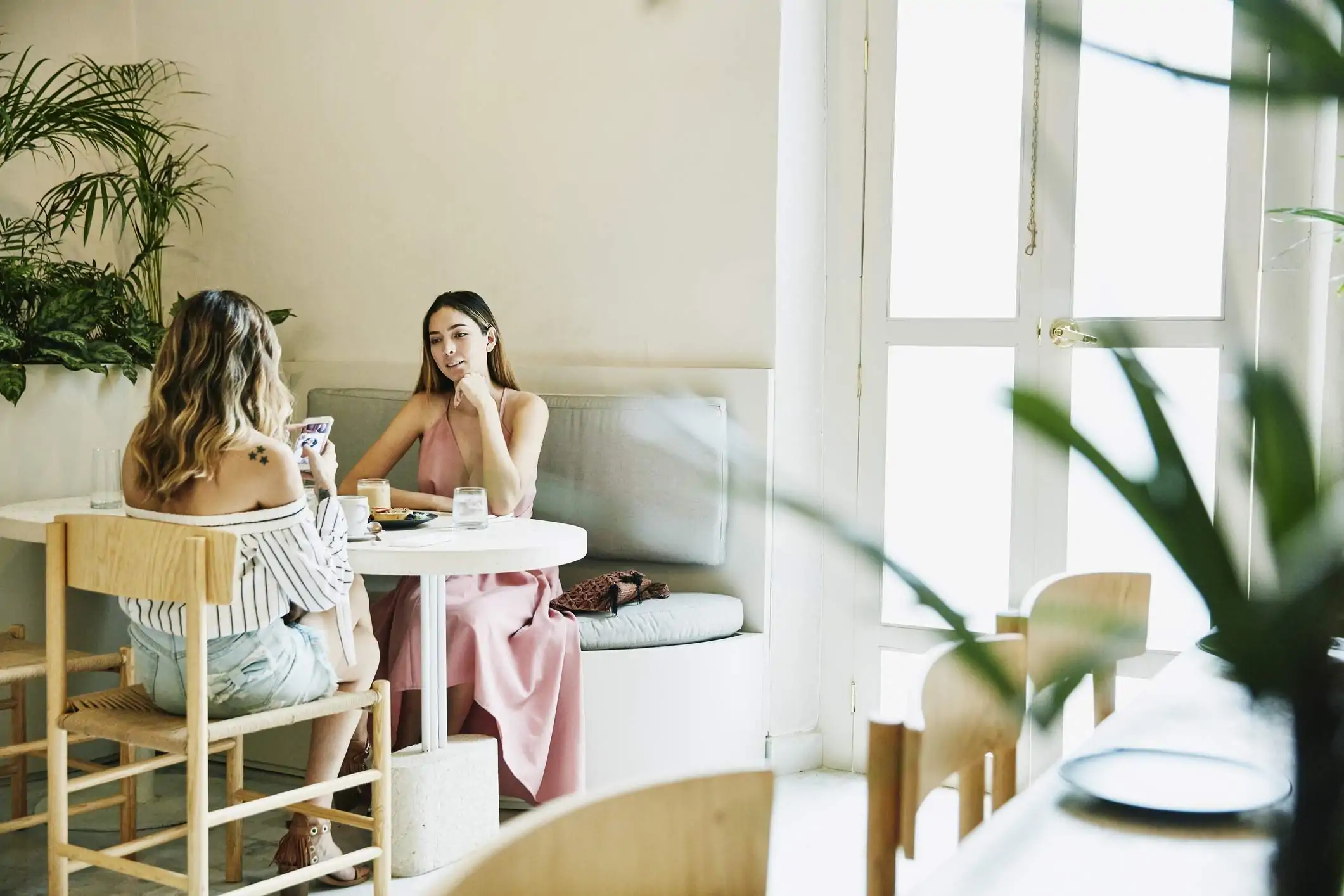 Image depicts two diners sitting at a booth in a restaurant, one of which is using their phone.