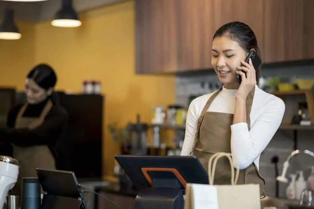 A waitress at a restaurant speaking on the phone while typing on a tablet