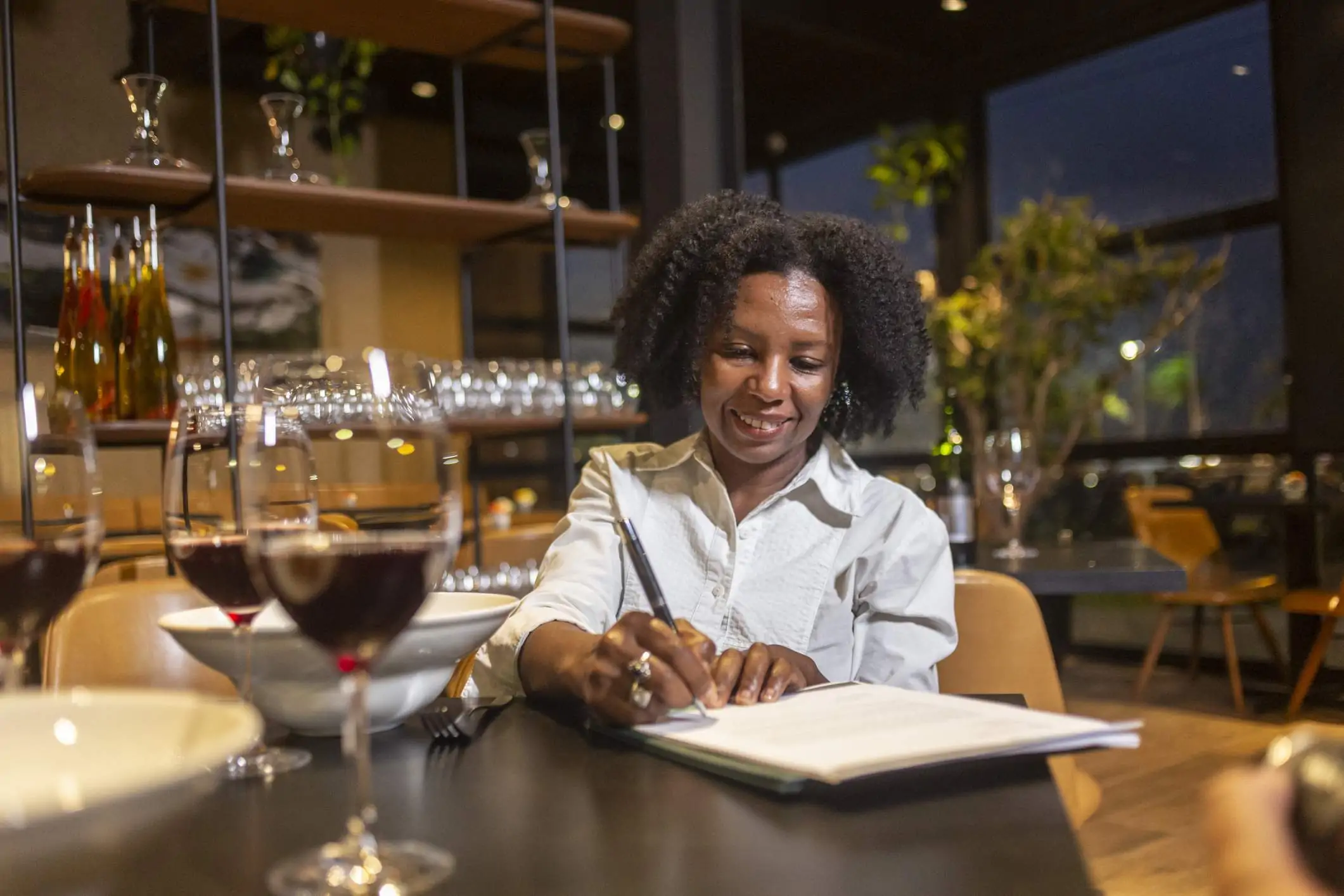 A restaurant owner is sitting at a restaurant table and writing down on a piece of paper.